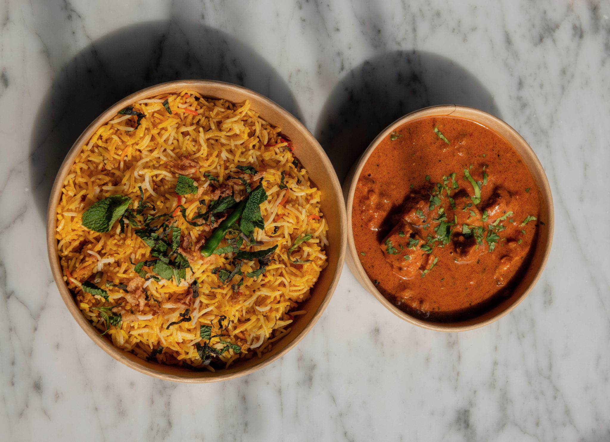 Een kom gekruide rijst en een kom curry op een lichte tafel.