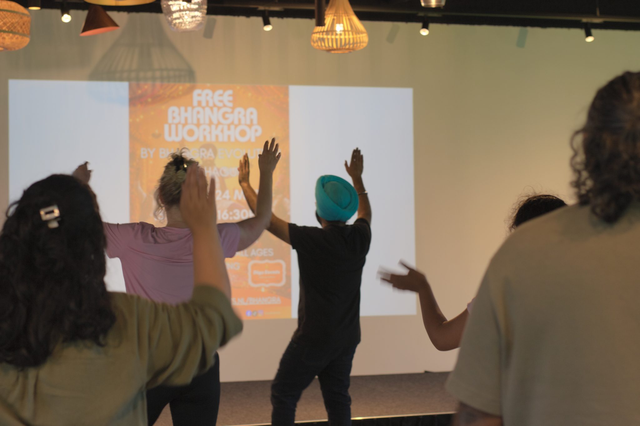 Deelnemers van achteren tijdens een dansworkshop, met geheven armen.