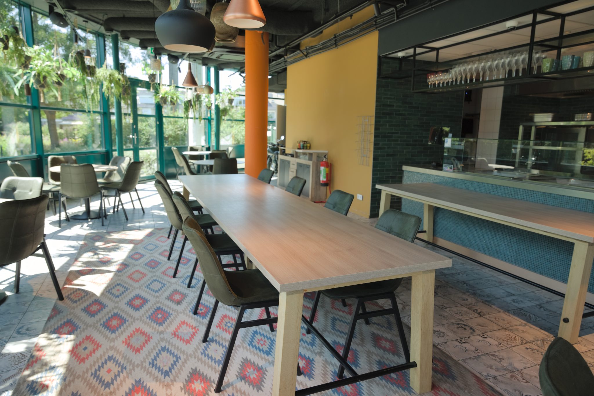 Lange houten tafel naast de bar en ramen van het restaurant.